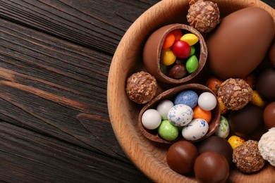 Photo of Tasty chocolate eggs and sweets in bowl on wooden table, top view. Space for text
