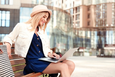 Photo of Beautiful woman using laptop on bench in city