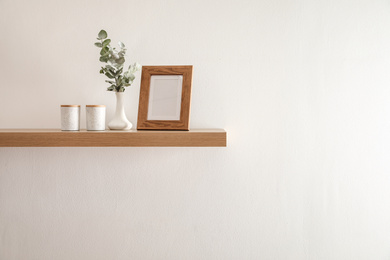 Wooden shelf with photo frame and decorative elements on light wall