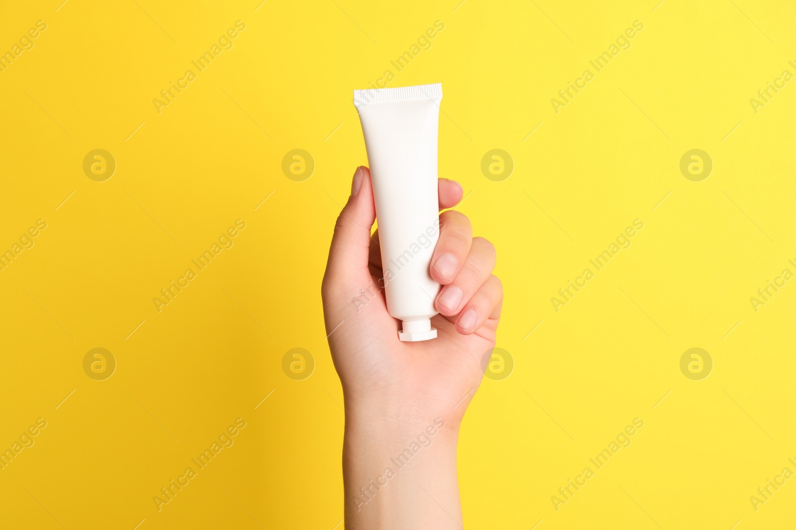 Photo of Woman holding tube of face cream on yellow background, closeup