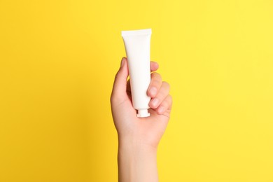 Photo of Woman holding tube of face cream on yellow background, closeup