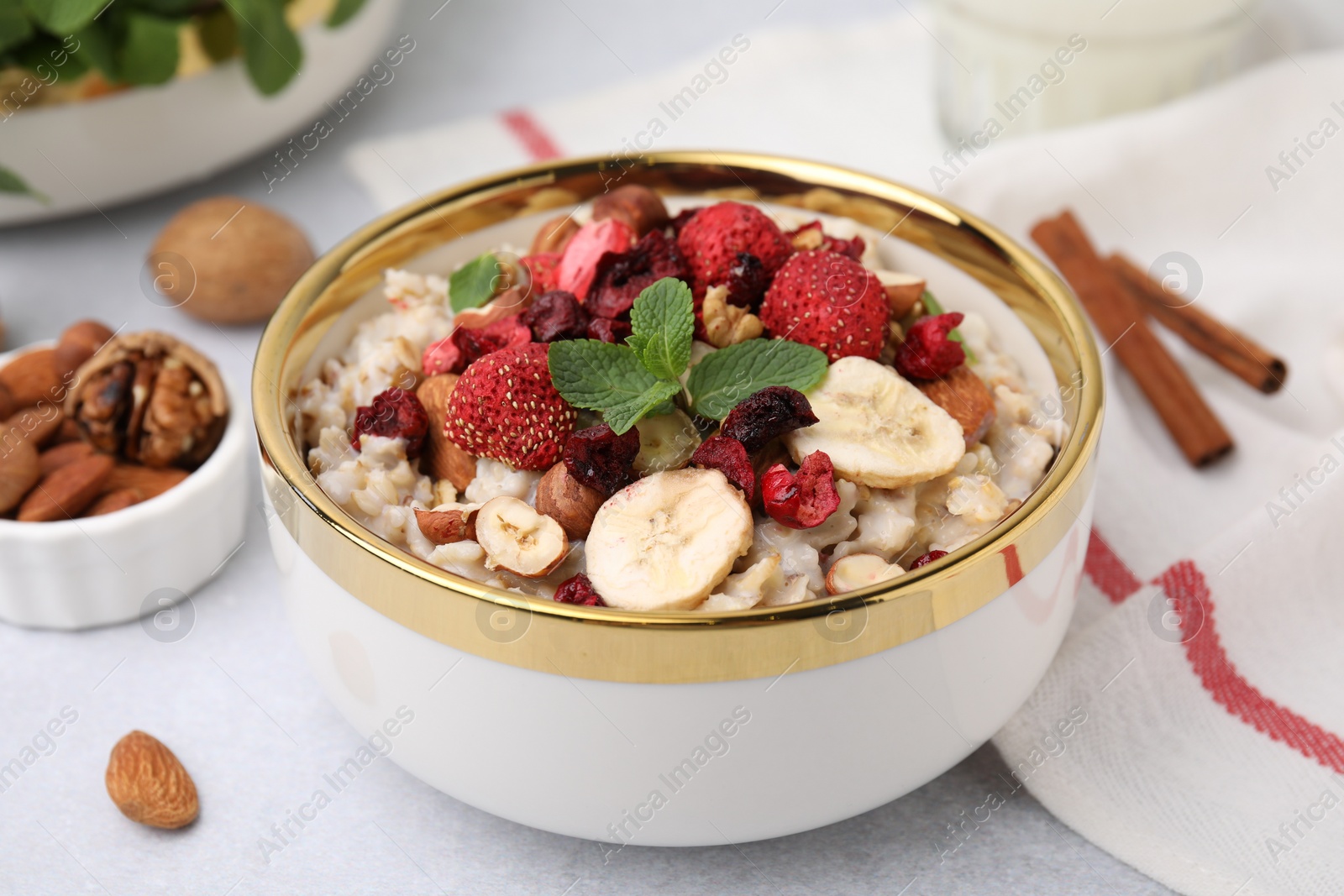 Photo of Delicious oatmeal with freeze dried berries, banana, nuts and mint on white table, closeup