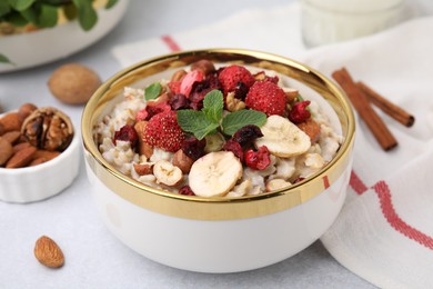 Photo of Delicious oatmeal with freeze dried berries, banana, nuts and mint on white table, closeup