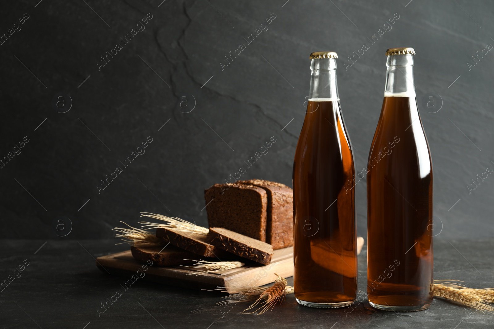 Photo of Bottles of delicious fresh kvass, spikelets and bread on grey table. Space for text