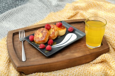 Photo of Tasty breakfast served in bedroom. Cottage cheese pancakes with fresh raspberries and sour cream on wooden tray