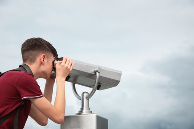 Photo of Teenage boy looking through mounted binoculars under sky. Space for text