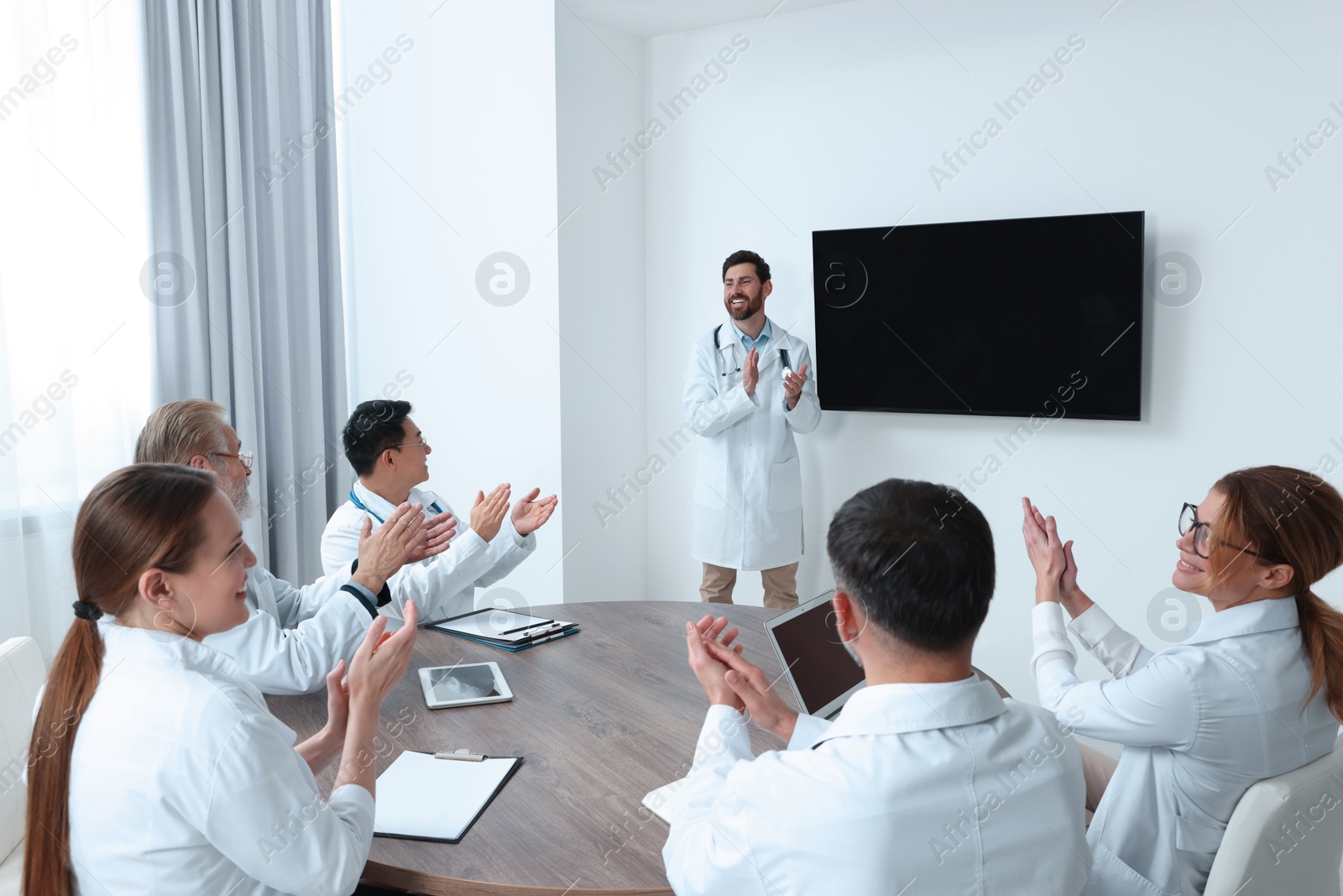 Photo of Team of doctors listening to speaker report near tv screen in meeting room. Medical conference