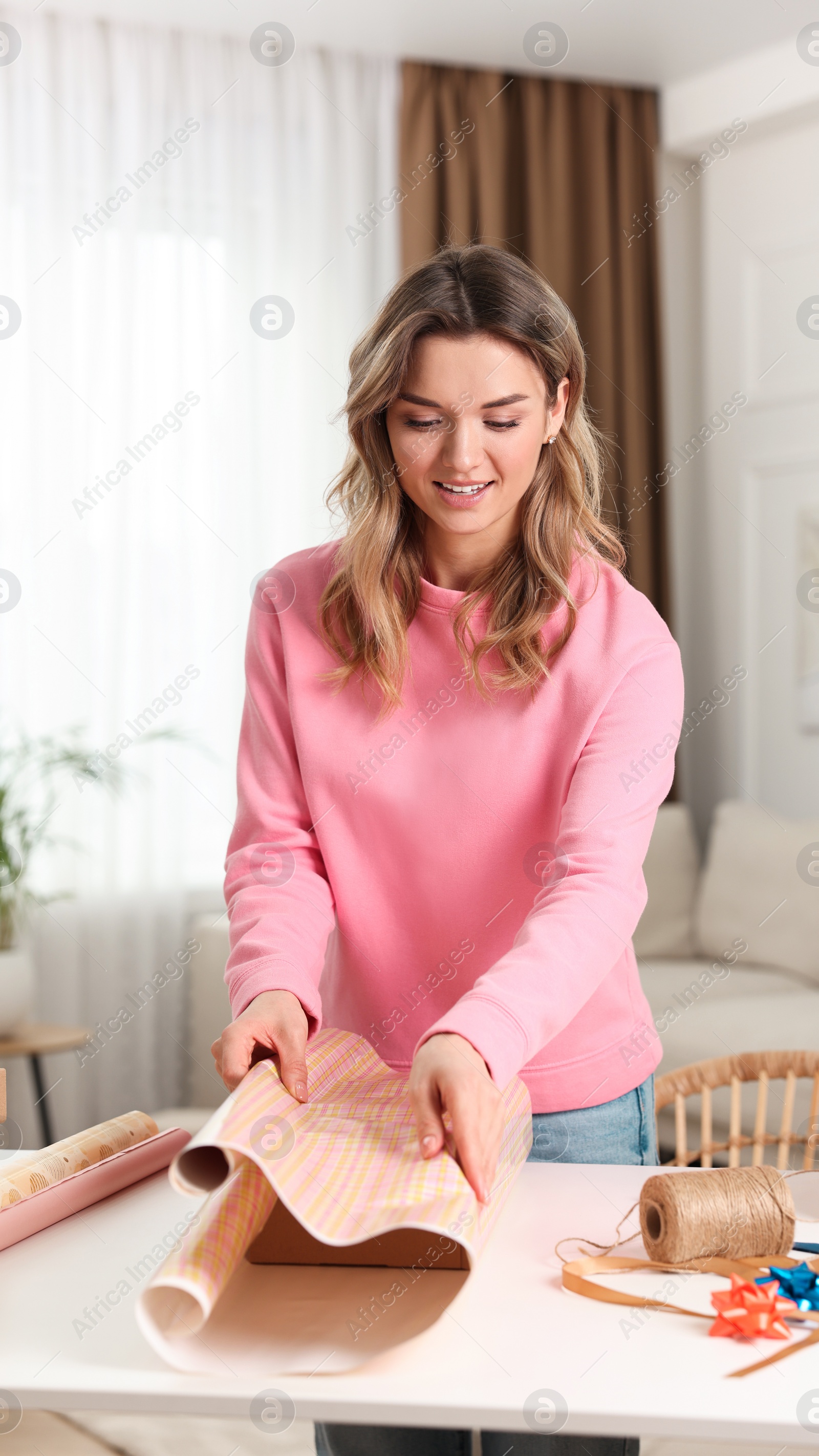 Photo of Beautiful young woman wrapping gift at table in living room