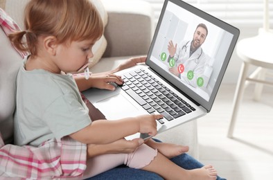 Mother and daughter having online consultation with pediatrician via laptop on sofa at home