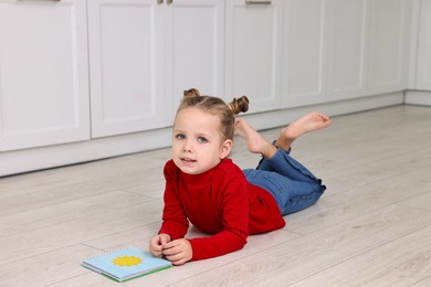 Photo of Cute little girl with book on warm floor in kitchen. Heating system