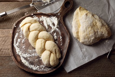 Photo of Raw braided bread and flour on wooden table, flat lay. Traditional Shabbat challah