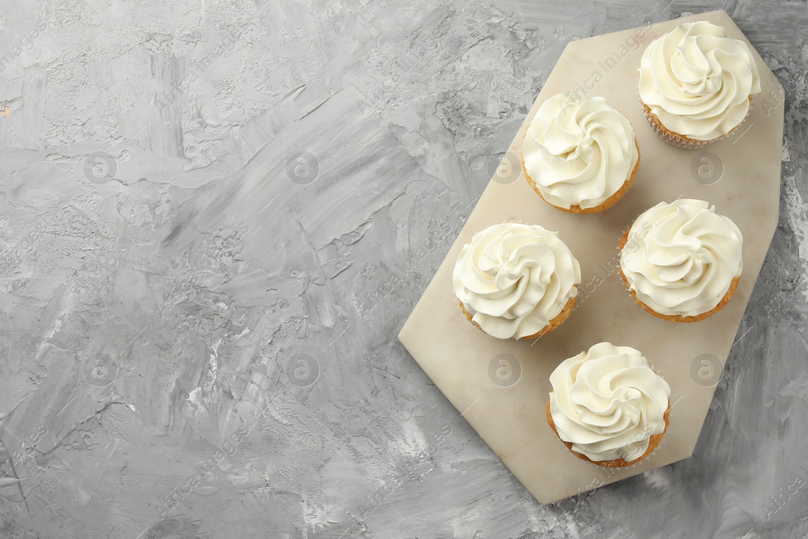 Photo of Tasty cupcakes with vanilla cream on grey table, top view. Space for text