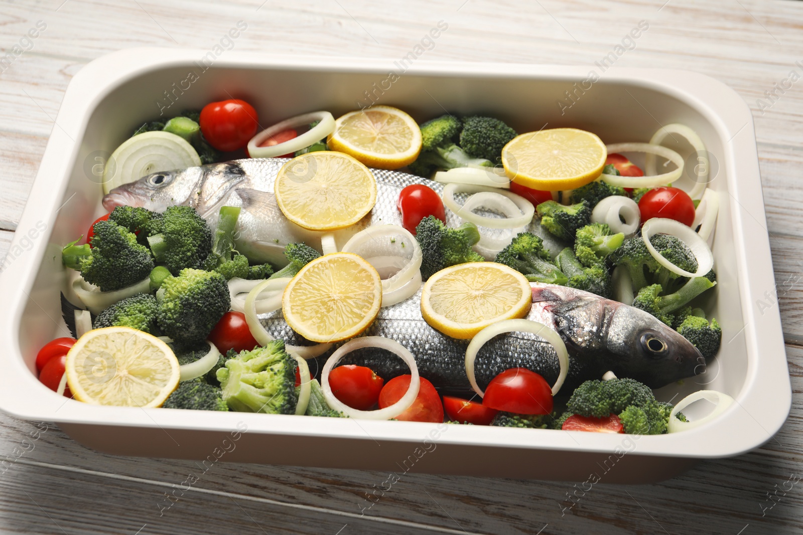 Photo of Raw fish with vegetables and lemon in baking dish on wooden table