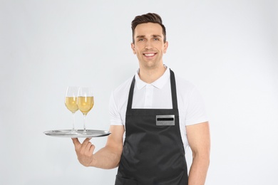 Photo of Handsome waiter holding tray with glasses of wine on light background