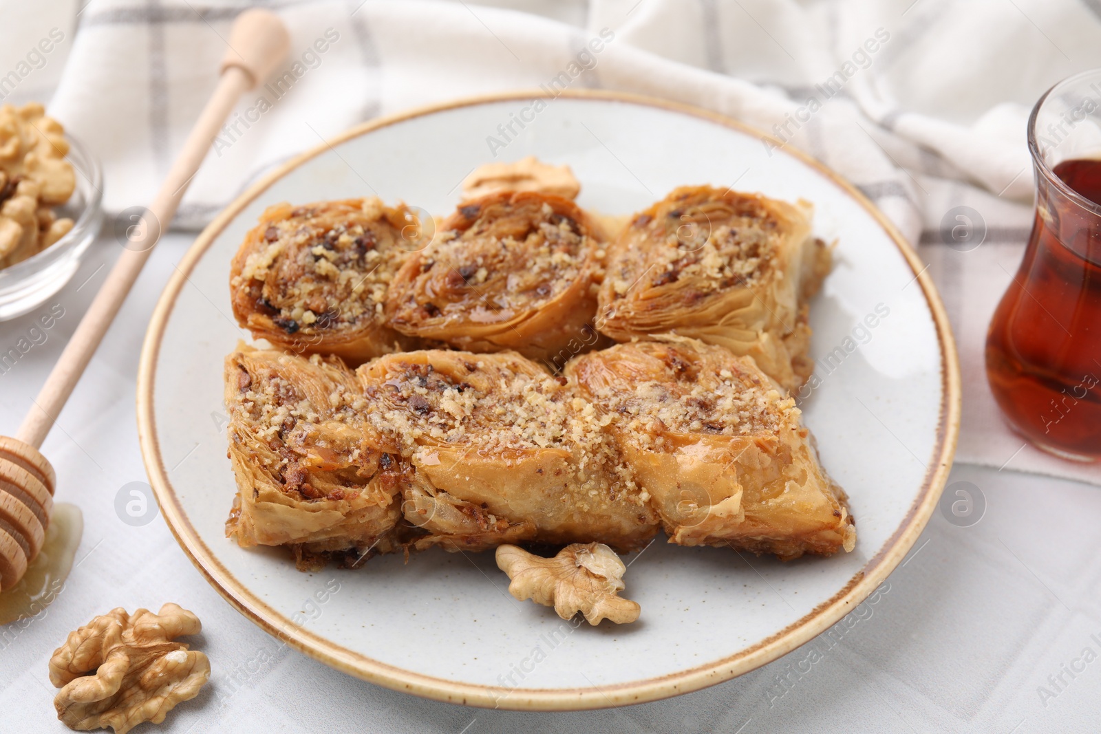 Photo of Eastern sweets. Pieces of tasty baklava, walnuts and tea on white tiled table, closeup