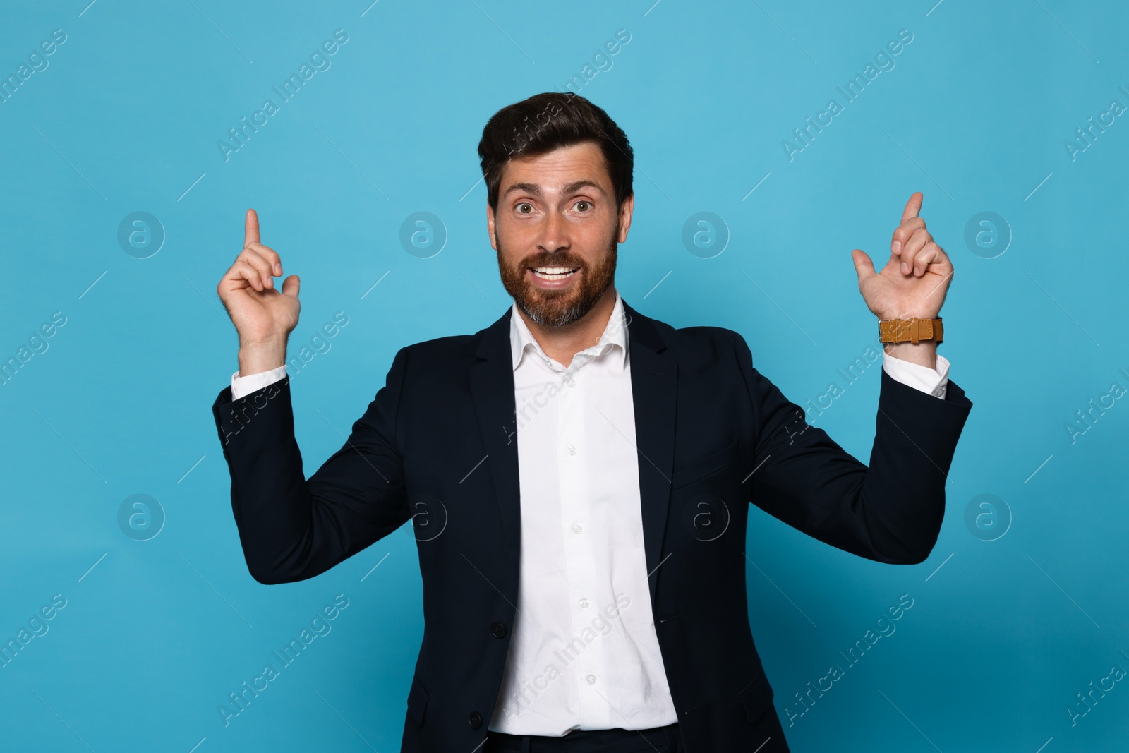 Photo of Smiling bearded man pointing index fingers up on light blue background