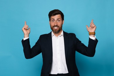Photo of Smiling bearded man pointing index fingers up on light blue background