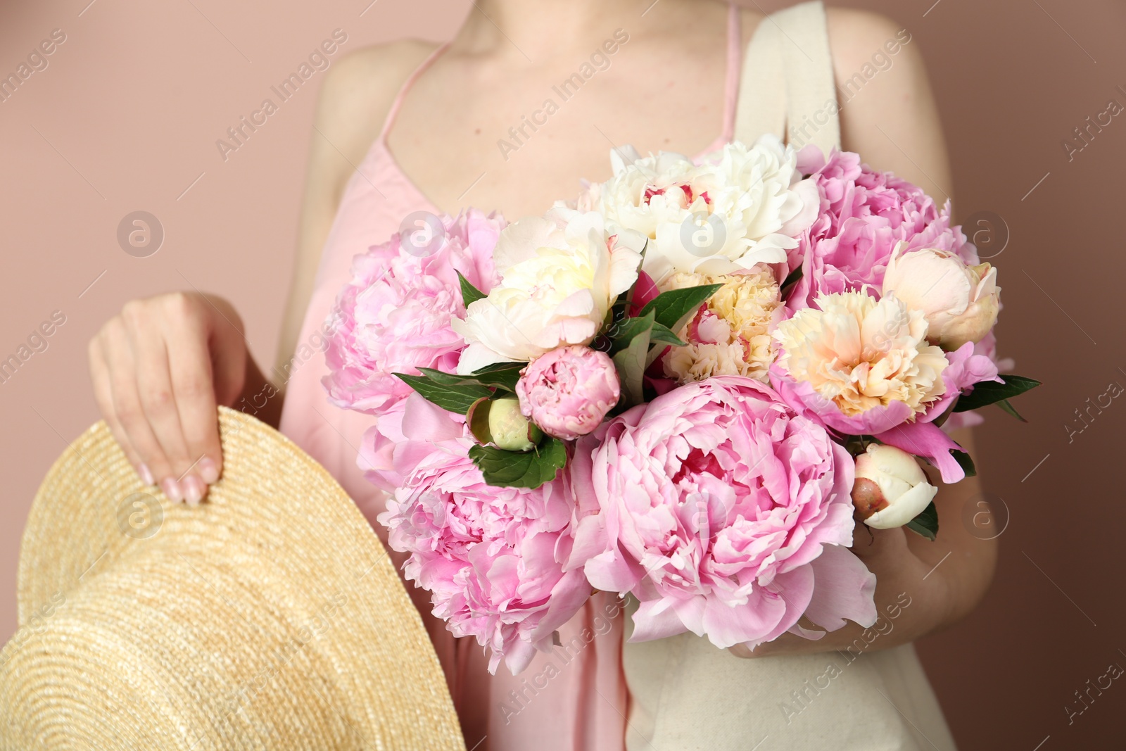 Photo of Woman with bouquet of beautiful peonies in bag and hat on beige background, closeup