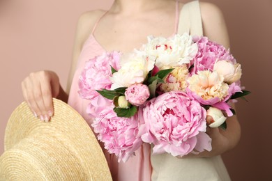 Photo of Woman with bouquet of beautiful peonies in bag and hat on beige background, closeup