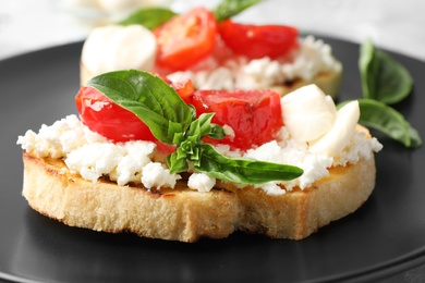 Tasty fresh tomato bruschettas on black plate, closeup