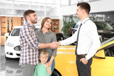 Photo of Young man shaking hands with salesman in car salon