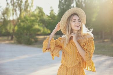Photo of Beautiful young woman in stylish yellow dress and straw hat outdoors