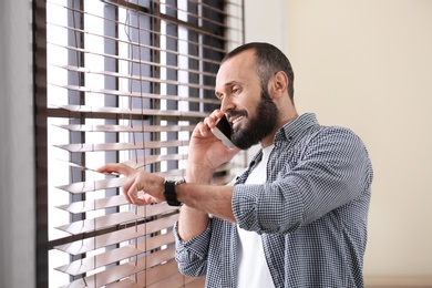 Photo of Portrait of handsome mature man talking on mobile phone near window indoors