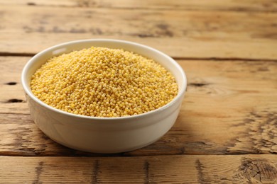 Photo of Millet groats in bowl on wooden table, space for text