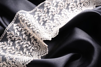 Photo of Beautiful white lace on black fabric, closeup