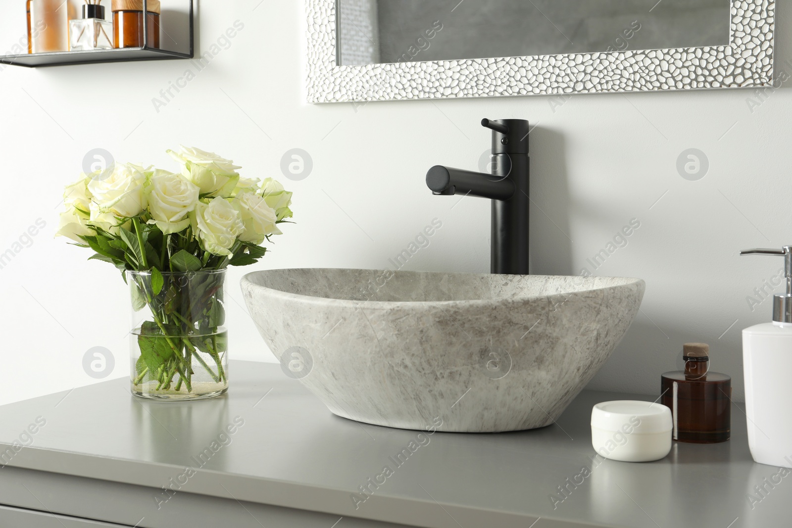 Photo of Vase with beautiful white roses and toiletries near sink in bathroom