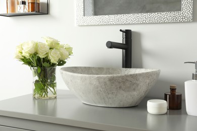 Photo of Vase with beautiful white roses and toiletries near sink in bathroom