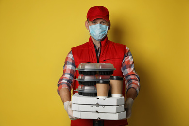 Courier in protective mask and gloves holding order on yellow background. Food delivery service during coronavirus quarantine