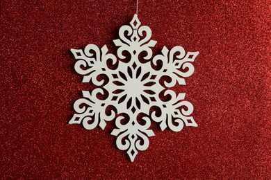 Photo of Beautiful decorative snowflake hanging on sparkling red glitter background, closeup