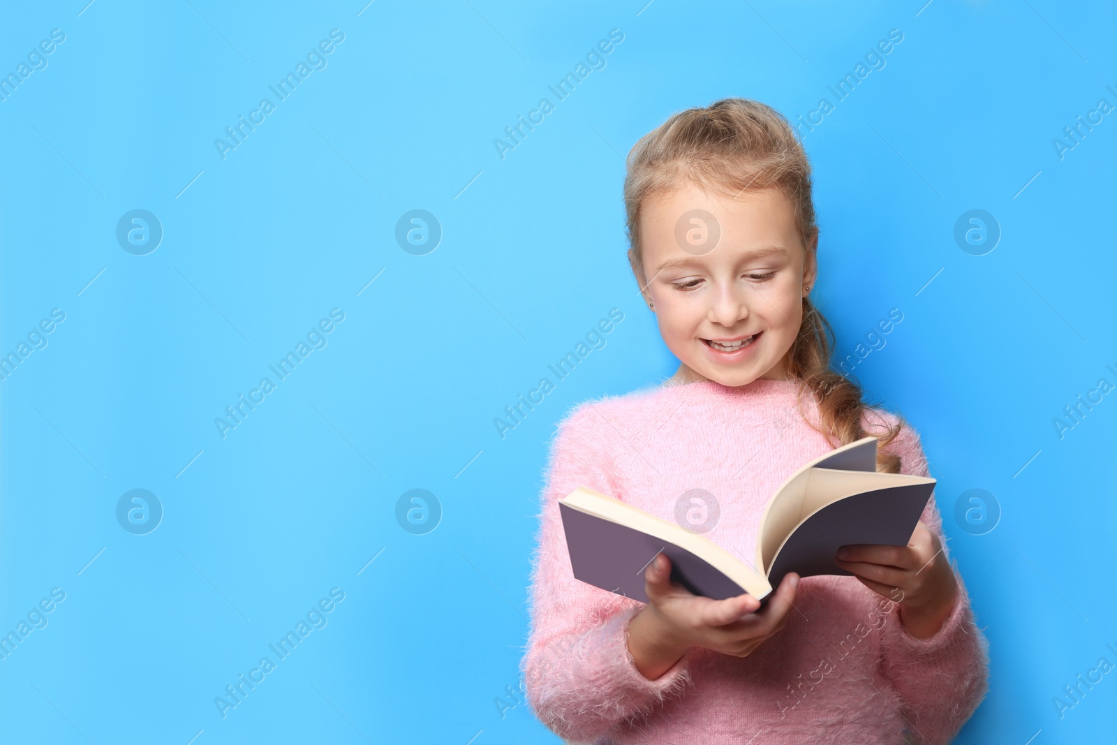 Photo of Happy little girl reading book on light blue background. Space for text