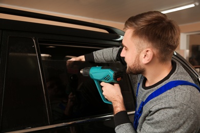 Worker tinting car window with heat gun in shop