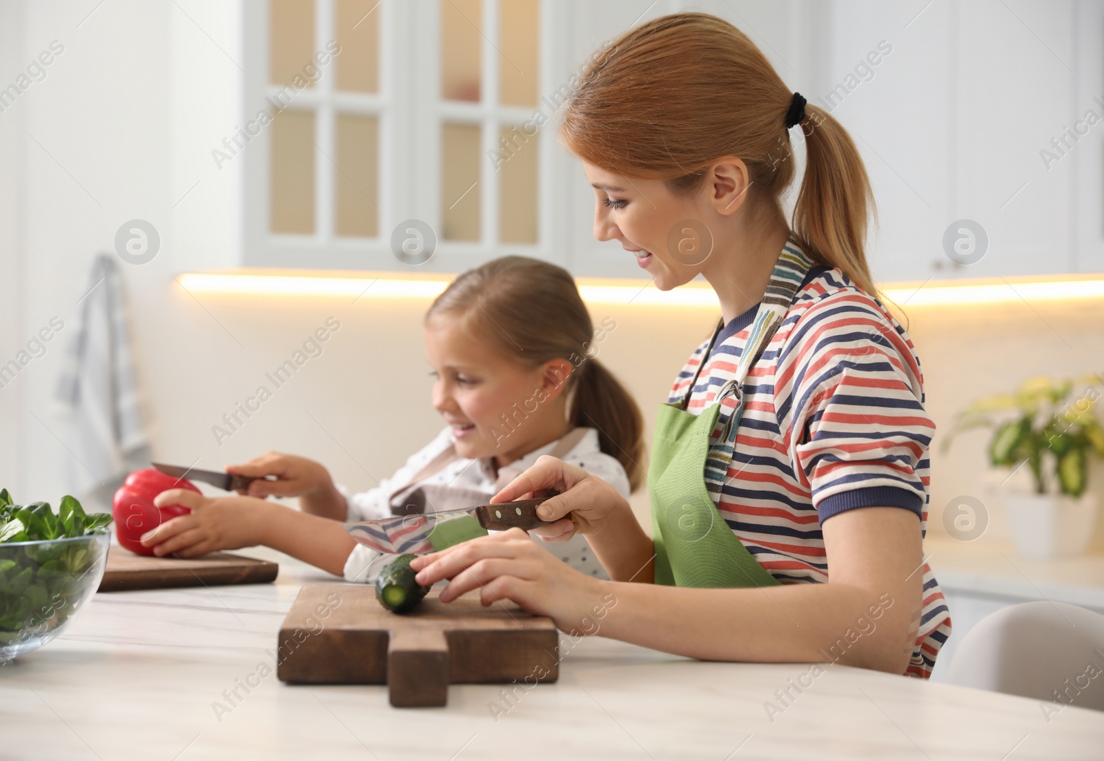 Photo of Mother and daughter cooking salad together in kitchen