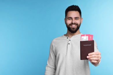 Photo of Happy man showing passport and tickets on light blue background. Space for text