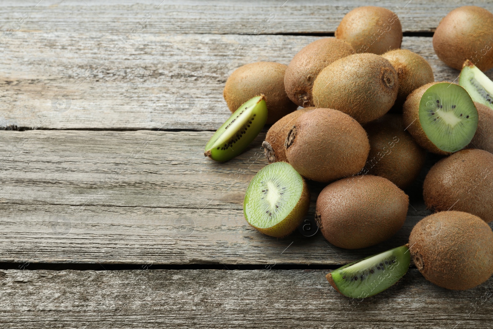 Photo of Pile of fresh ripe kiwis on wooden table, space for text