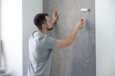 Photo of Man hanging stylish gray wallpaper in room