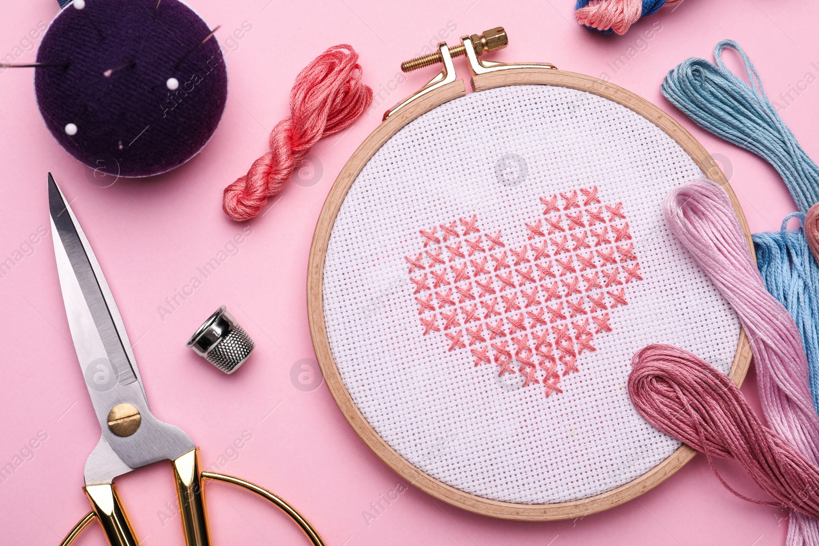 Photo of Flat lay composition with embroidery and different sewing accessories on pink background