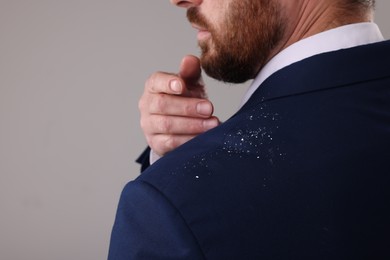 Man swiping dandruff of his suit against grey background, closeup. Space for text