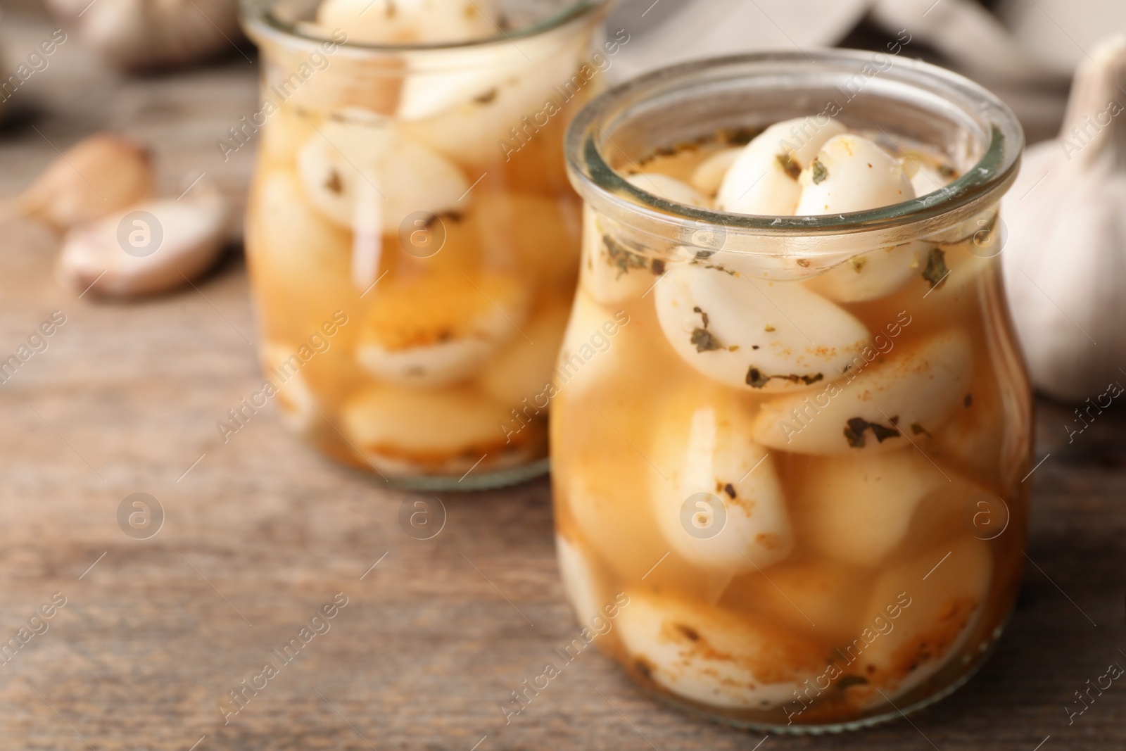 Photo of Preserved garlic in glass jar on wooden table, closeup. Space for text