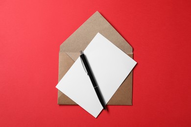 Photo of Blank sheet of paper, letter envelope and pen on red background, top view