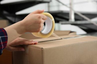 Photo of Woman taping cardboard box indoors, closeup view