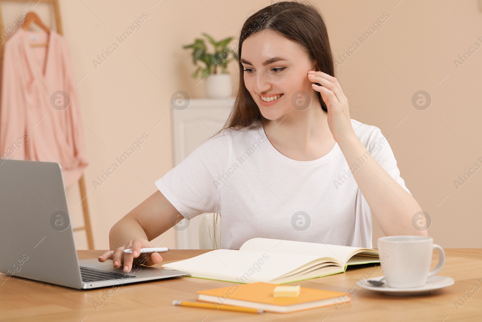 Photo of Woman with notebook working on laptop at wooden table indoors