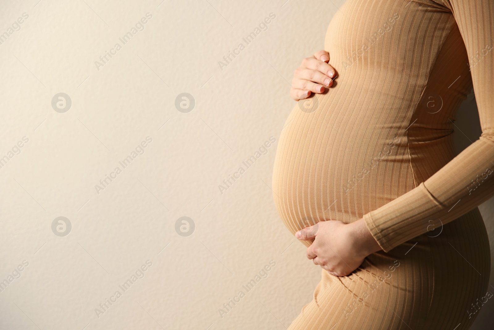 Photo of Pregnant woman touching her belly on beige background, closeup. Space for text