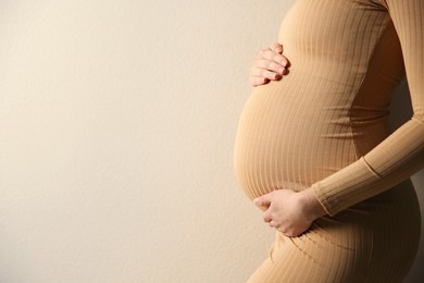 Pregnant woman touching her belly on beige background, closeup. Space for text