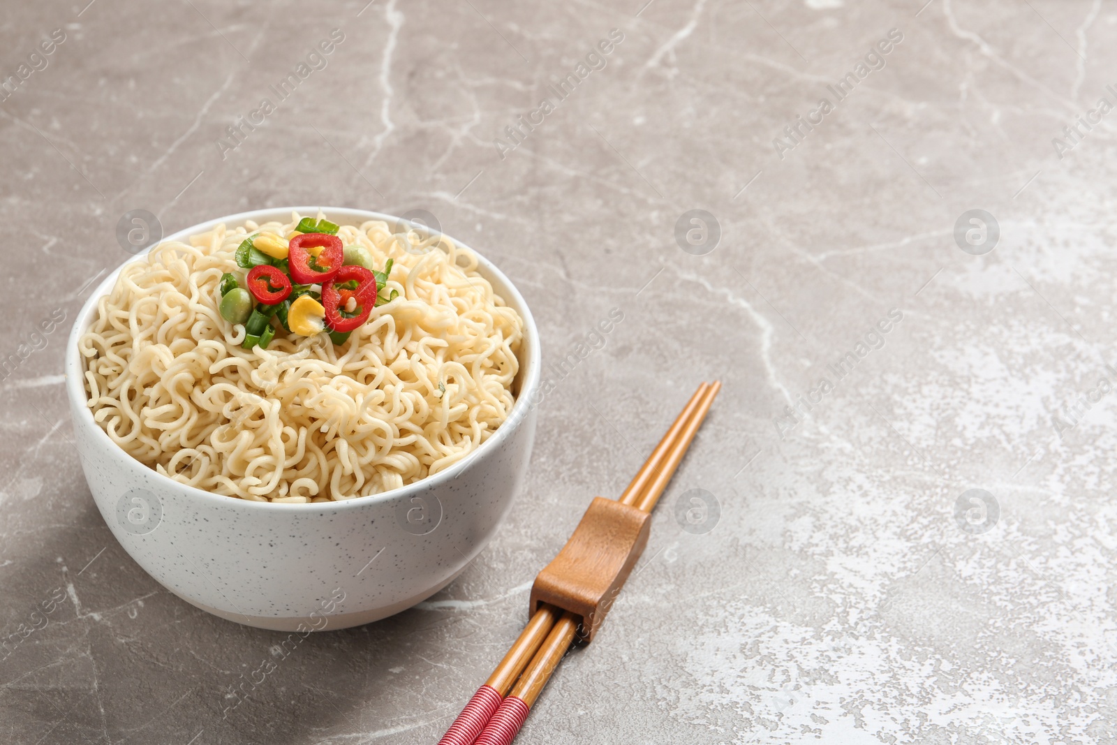 Photo of Bowl of noodles with vegetables and chopsticks served on table. Space for text