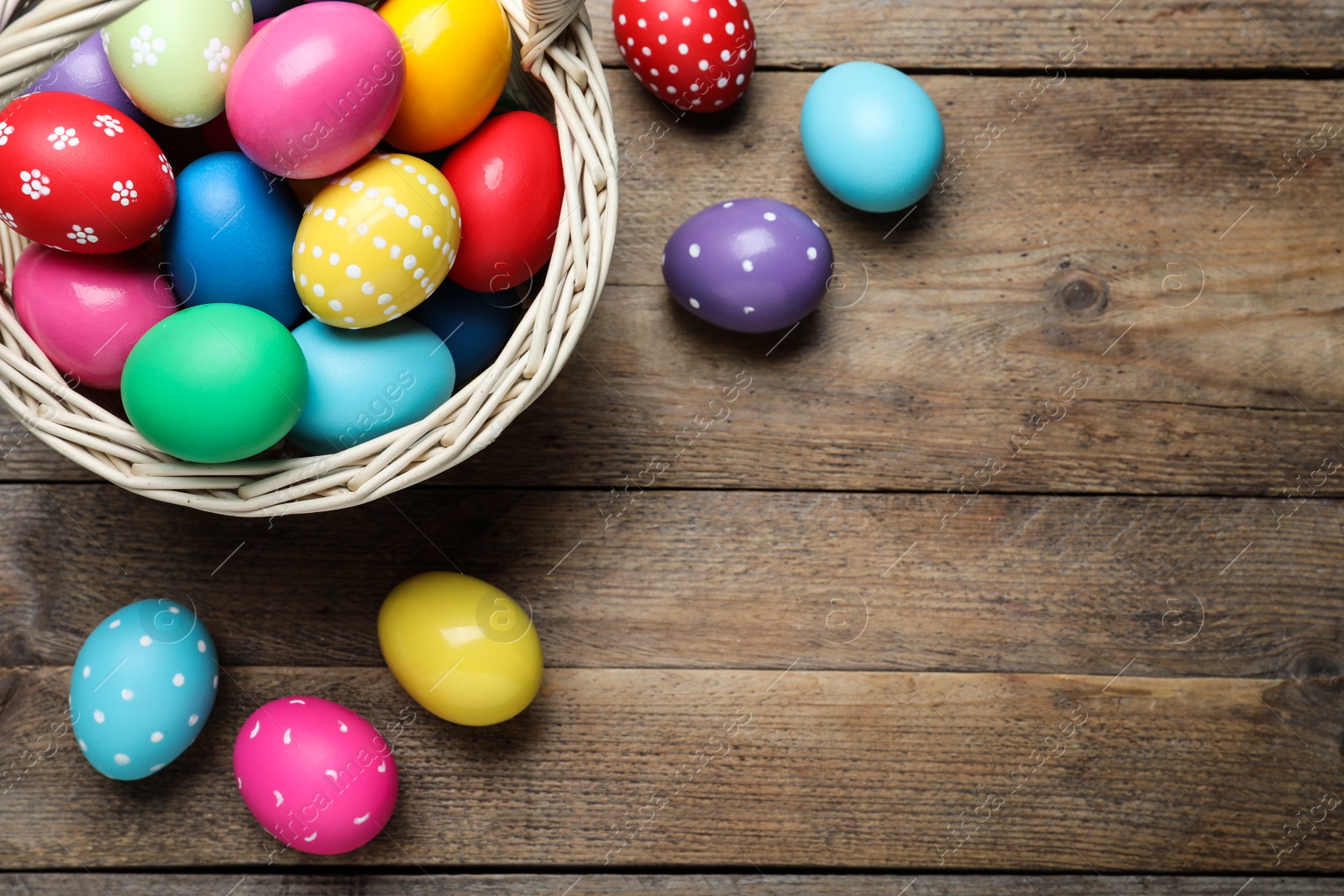 Photo of Colorful Easter eggs in wicker basket on wooden table, flat lay. Space for text