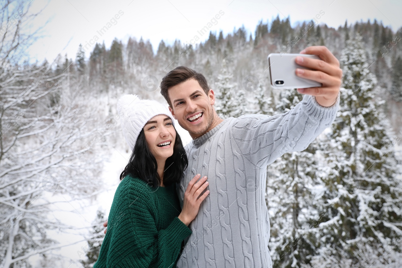 Photo of Happy couple in sweaters taking selfie near winter forest